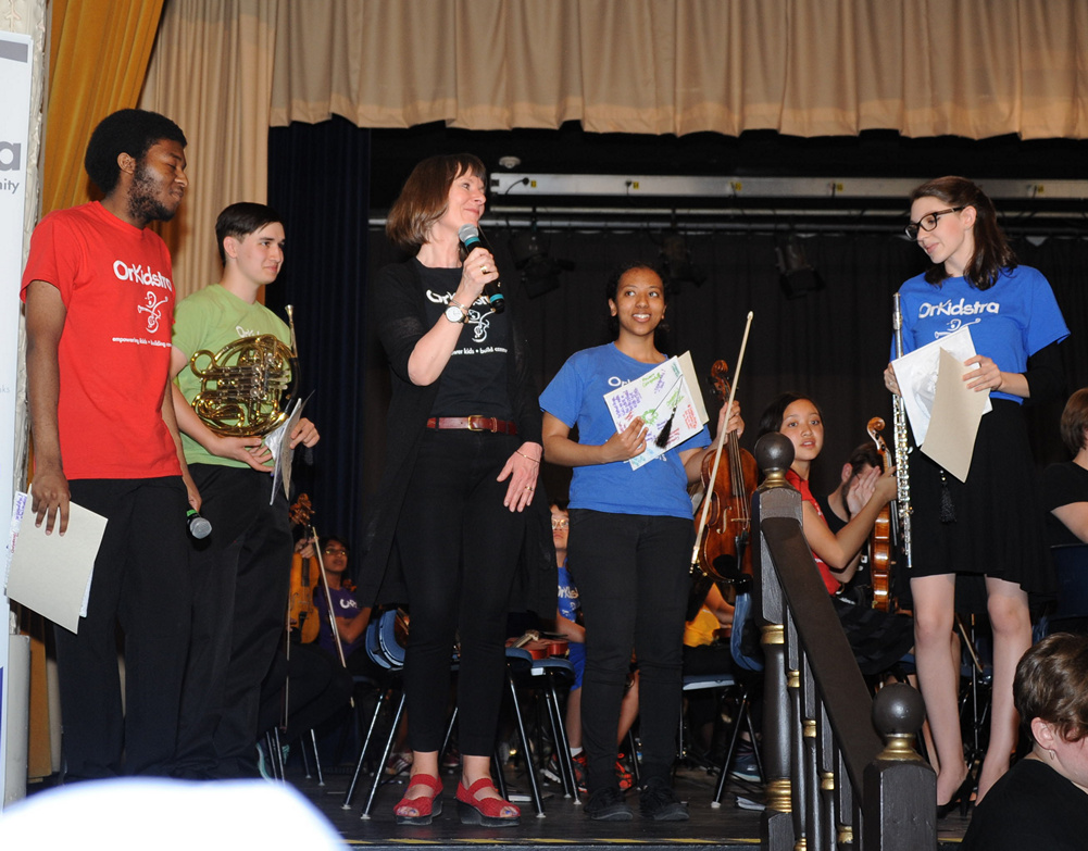 Four teens who are graduating from OrKidstra stand with one adult, Ms. Tina, who is looking very proud of them.